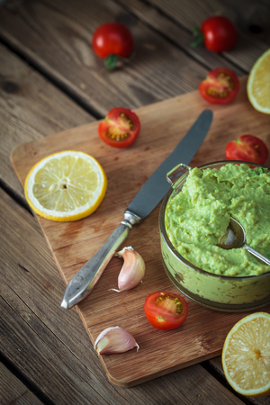 Guacamole on wooden table surrounded by its ingredientsの写真素材