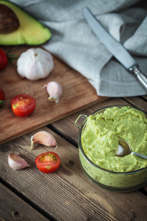 Guacamole on wooden table surrounded by its ingredientsの写真素材