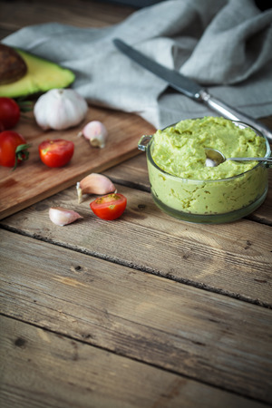 Guacamole on wooden table surrounded by its ingredientsの写真素材