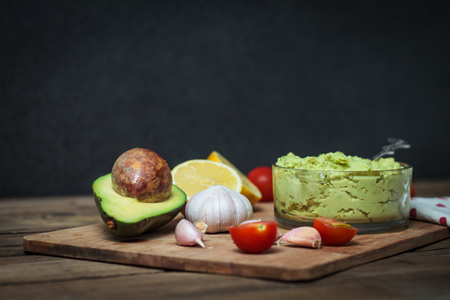 Guacamole on wooden table surrounded by its ingredientsの写真素材