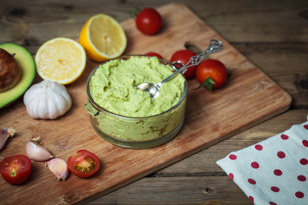 Guacamole on wooden table surrounded by its ingredientsの写真素材