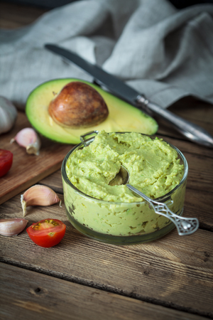 Guacamole on wooden table surrounded by its ingredientsの写真素材