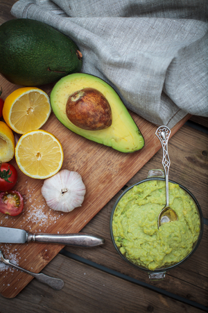 Guacamole on wooden table surrounded by its ingredientsの写真素材