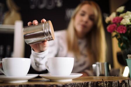 The girl adds cinnamon to the cup with coffee in cafe. Young woman barista working in coffee shopの写真素材