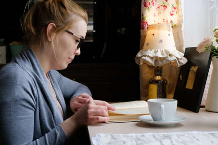 beautiful young woman reading interesting book while drinking tea at home, in cafe