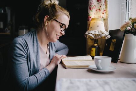 beautiful young woman reading interesting book while drinking tea at home, in cafe