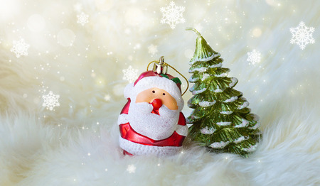 Small Santa Claus and Christmas tree on white fur, surrounded with glitter star dust and snowflakesの写真素材