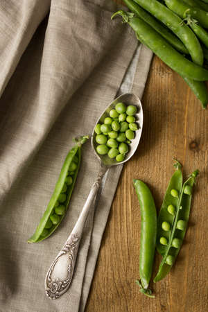 Wooden spoon with fresh green peas on table with a piece of apronの写真素材