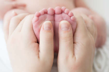 Tiny feet of a newborn baby in mother's hands on a white background. Front view