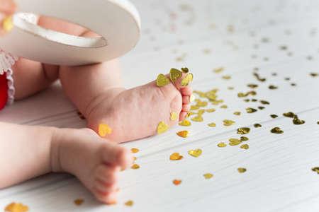 Baby feet on a festive white background with yellow sparkles in the form of a heart. Child holding a...