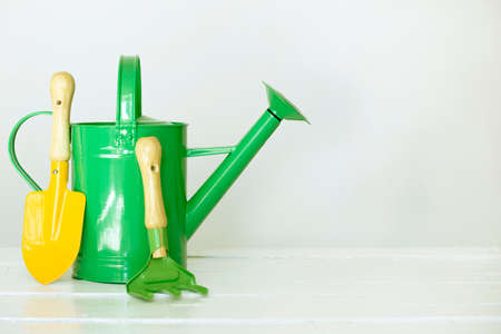 Colored kids gardening tools on a white wooden table. Watering can, shovel, rake. Front view. Copyspaceの写真素材