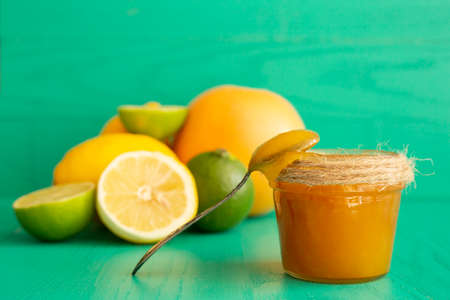 A jar of honey with a spoon on a wooden turquoise background with citrus fruits - orange, lime, lemon frontal viewの写真素材