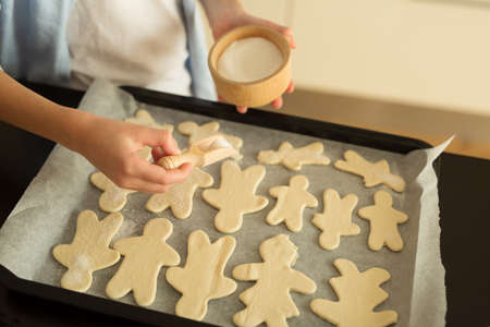 A child in a white T-shirt and a blue sweater sprinkles sugar on Christmas men before baking....