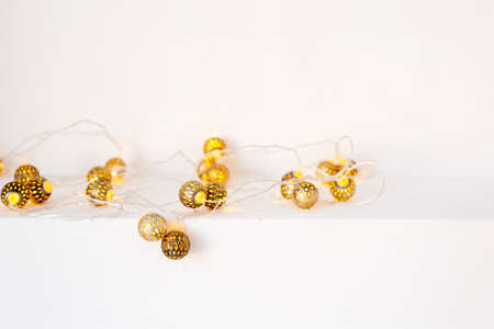 Metallic gold garland glowing with warm light on a white shelf on the wall. Front view. Holiday waiting conceptの写真素材