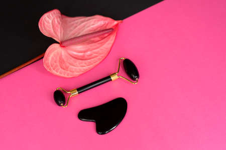 Onyx massage guasha scraper and face roller and Anthurium on pink and black background. Massage tool for facial skin care, SPA beauty treatment concept. Space for text. Flatlayの写真素材