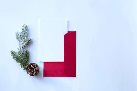 A red envelope with a blank white sheet of paper and New Years attributes - a pine cone, a twig of a Christmas tree. Concept of letter to santa or congratulations. View from above. Place for textの写真素材