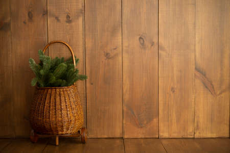 Juicy beautiful green branches of a Christmas tree in a wicker cart on a brown wooden background. Place for text. Front viewの写真素材