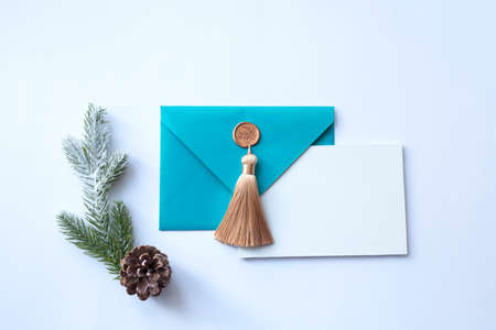 Turquoise envelope with a beautiful gold tassel and a white sheet of paper on a white background with a sprig of a Christmas tree and a pine cone. Flat lay. Place for textの写真素材