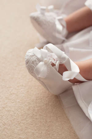Cute newborn baby feet in white booties on the beige background and white dressの写真素材
