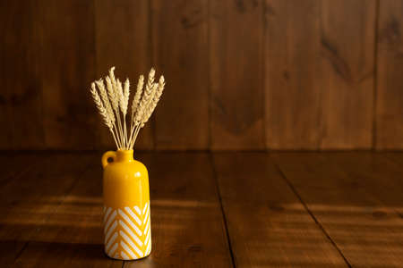 Dried natural spikelets in a yellow vase with white stripes on a brown wooden background with beautiful natural light and shadows - perfect for your design. There is free space for textの写真素材