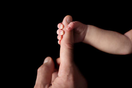 Tiny newborn hand holds fathers finger on the black background. Front wiev