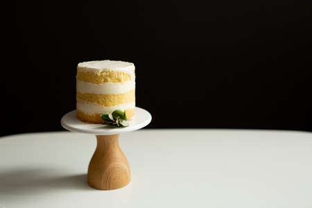 A tiny naked cake on a wooden stand with a brown base on a white table against a black background. Near the cake is eucalyptus. Place for textの写真素材