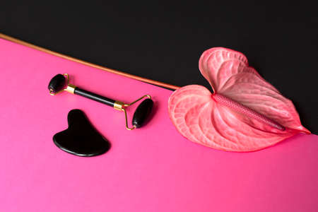 Onyx massage guasha scraper and face roller and Anthurium on pink and black background. Massage tool for facial skin care, SPA beauty treatment concept. Space for text. Flatlayの写真素材