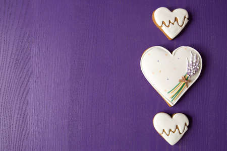 Three gingerbread hearts depicting heart rate and lavender on a lilac wooden background. Love and valentines day concept. There is room for text. View from aboveの写真素材