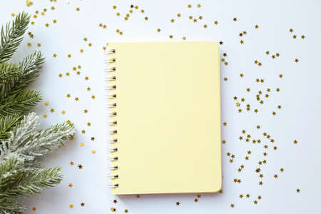Yellow blank notepad on spirals on a festive white christmas background with gold sparkles. View from above. Place for your text. Ideal for New Yearの写真素材