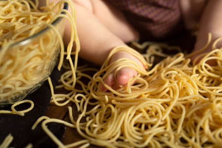 Little chubby Kids foot in pasta on a wooden brown background, table. Feeding concept. Spaghetti smash conceptの写真素材