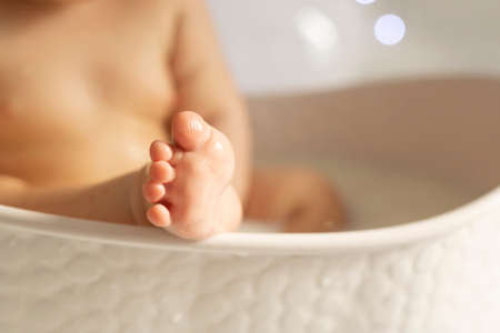 A tiny baby foot on the edge of the tub. Baby in the bath. Care procedures for childrenの写真素材