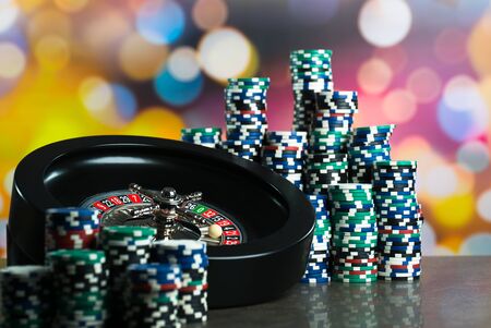 High contrast image of casino roulette, poker game, dice game, poker chips on a gaming table, all on colorful bokeh background.の写真素材
