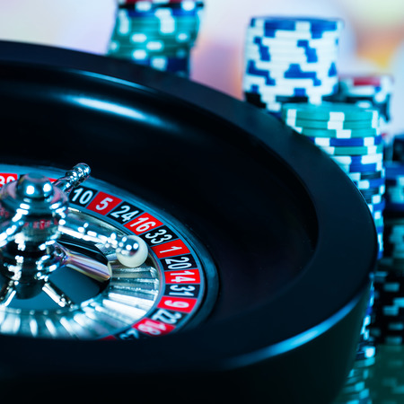 High contrast image of casino roulette and poker chips on bokeh background.
