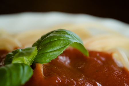 Italian spaghetti pasta topped with a tomato and fresh basilの写真素材