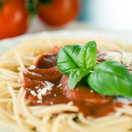Italian spaghetti pasta topped with a tomato and fresh basilの写真素材