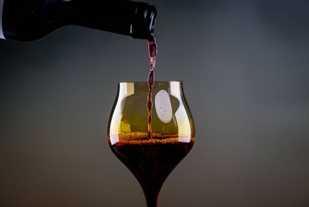 Pouring red wine from a bottle into a wineglass: wine tasting and celebrationの写真素材