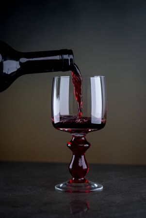 Pouring red wine from a bottle into a wineglass: wine tasting and celebrationの写真素材
