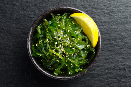 Top view of a bowl of chuka seaweed salad with sesame seeds and lemon slice.の素材