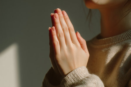 Side view of young woman's hands pressed together in prayer gesture indoors.の素材