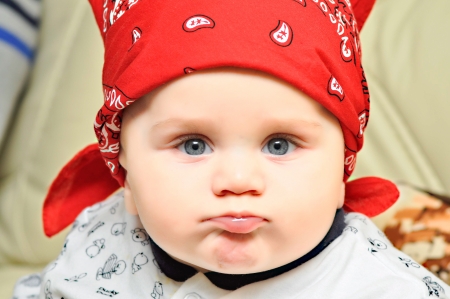Baby boy with blue eyes and red scarf on the head grimacingの写真素材