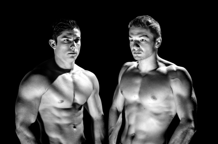 Two muscular men  showing their muscles against black background
の写真素材
