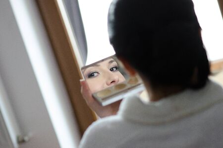 Young beautiful bride finishing her makeup before wedding - face reflection