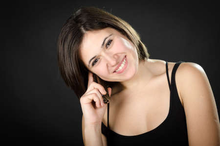 Portrait of young beautiful woman speaking on  phone against black background
