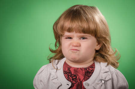 Portrait of litlle girl being angry  against green background