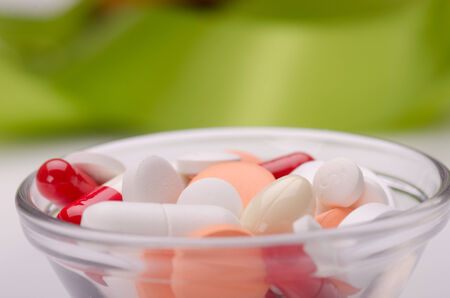 Different pills in a bowl on white surface against green background