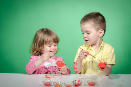 Happy children   painting Easter eggs against green backgroundの写真素材