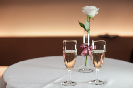 Two glasses with champagne and a white rose on a white tableの写真素材
