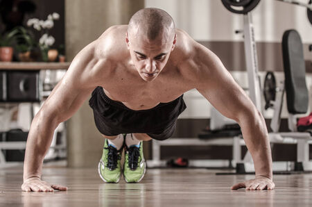 Muscular man doing push ups in a gym