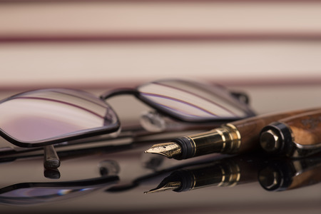 Fountain pen and reading glasses and a black glossy surfaceの写真素材