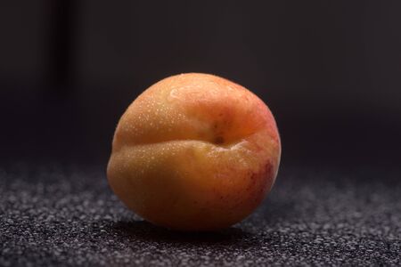 Apricot with water drops on a black reflective surfaceの写真素材